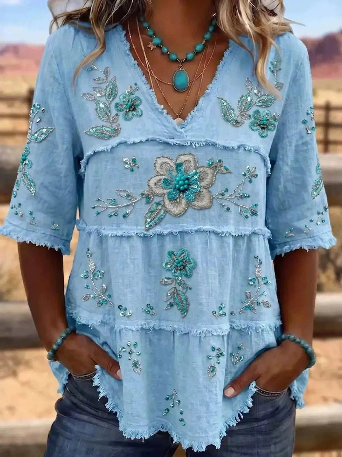 Full Size Floral light blue polyester blouse with embroidered flowers, tiered panels, V-neck, and raw hems